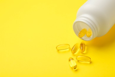 Photo of Softgel capsules and bottle on yellow background, closeup. Space for text