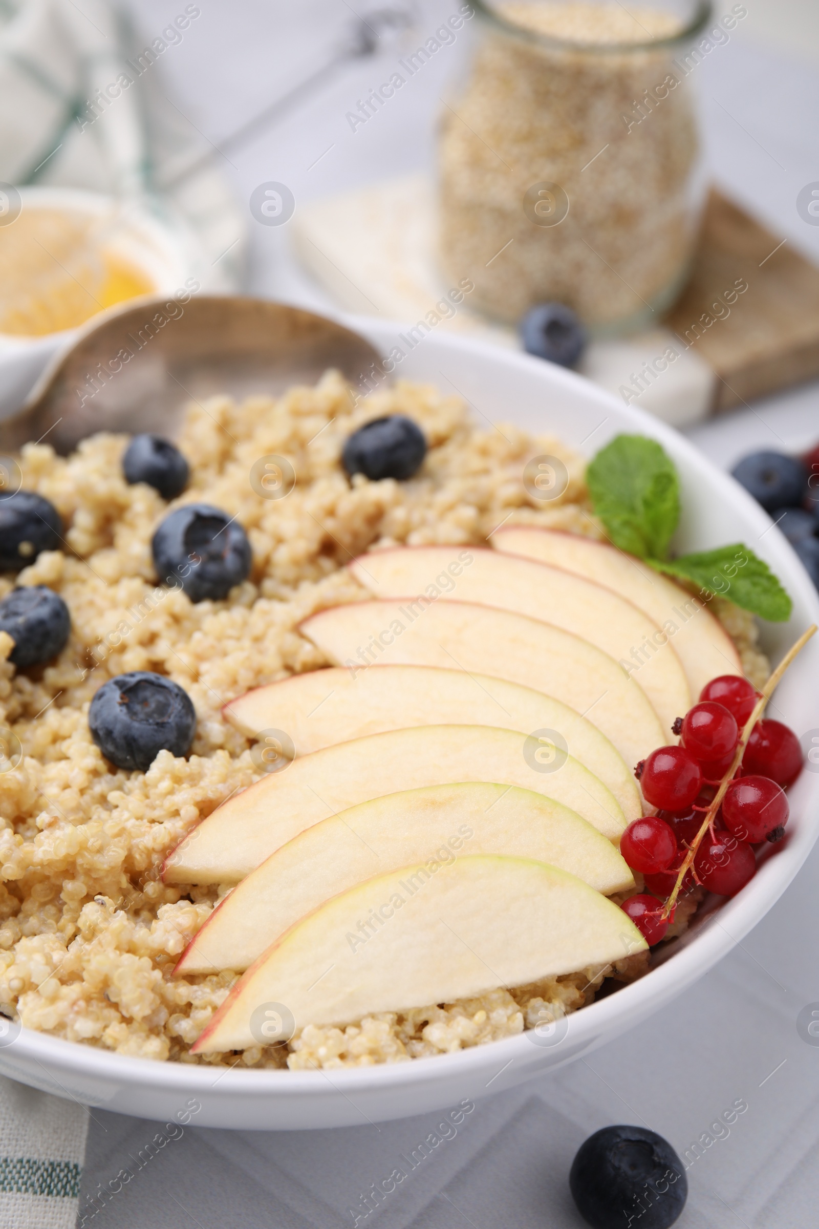 Photo of Bowl of delicious cooked quinoa with apples, blueberries and cranberries on white tiled table, closeup