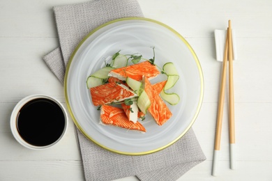 Photo of Fresh crab sticks with cucumber served on white wooden table, flat lay