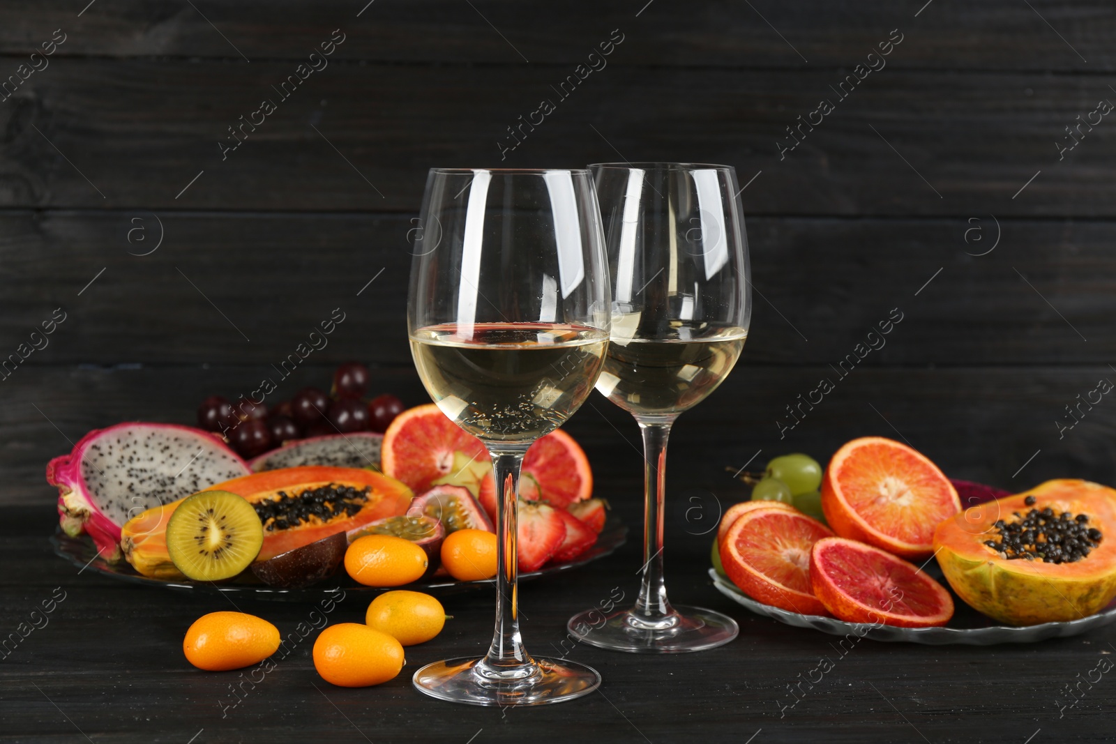 Photo of Delicious exotic fruits and wine on black wooden table