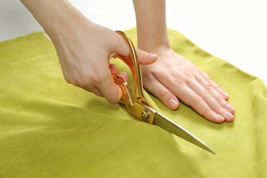 Seamstress cutting light green fabric with scissors at workplace, closeup