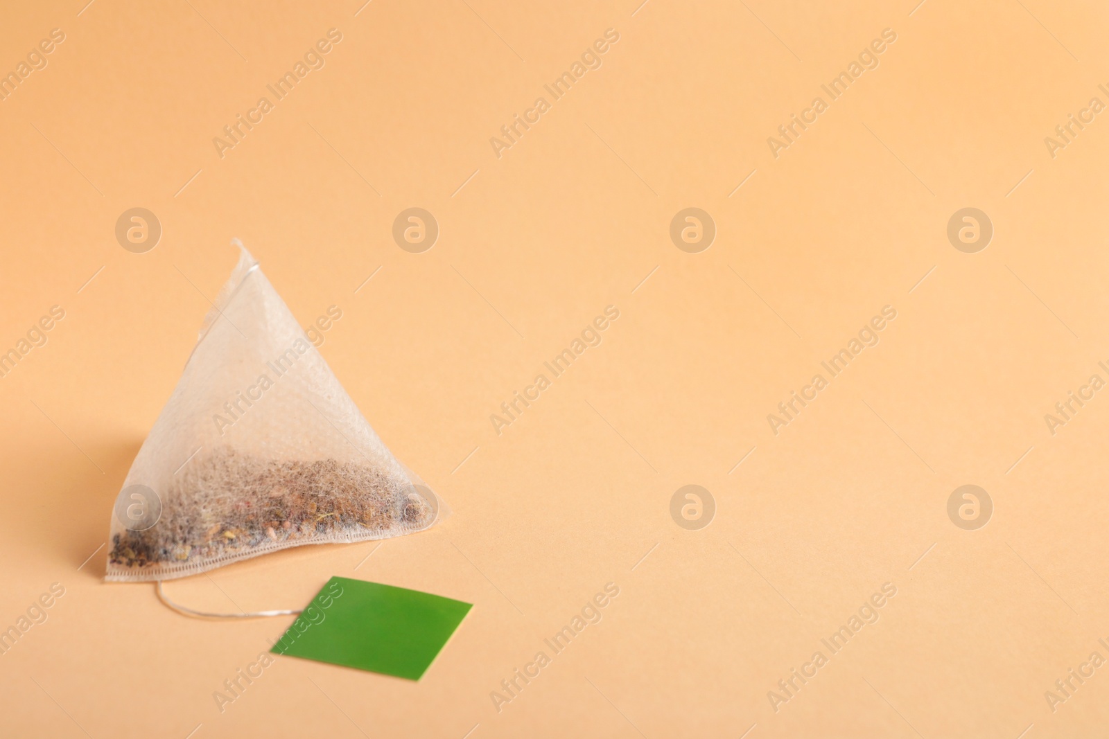 Photo of Paper tea bag with tag on beige background, space for text