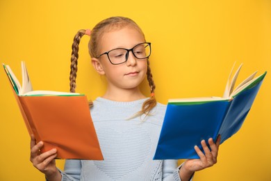 Cute little girl with glasses and textbooks on yellow background