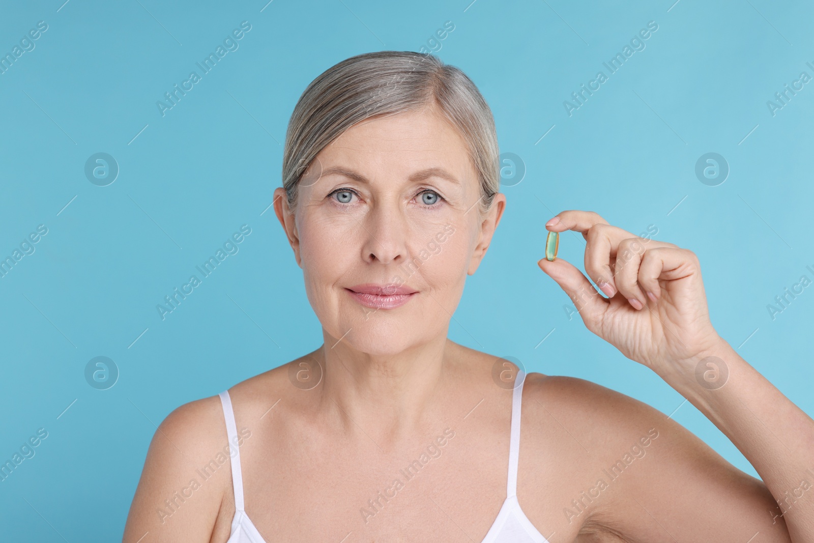 Photo of Beautiful woman with vitamin capsule on light blue background