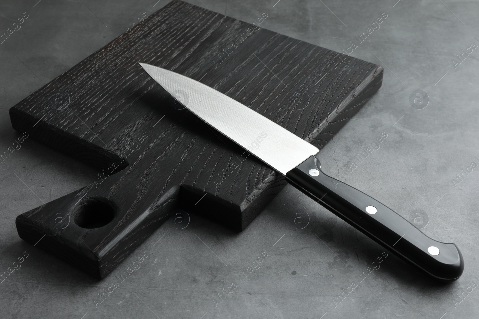 Photo of Knife and black wooden board on grey textured table