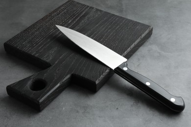 Photo of Knife and black wooden board on grey textured table