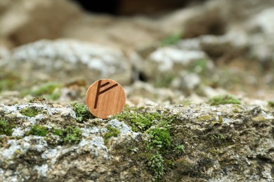 Wooden rune Fehu on stone with moss outdoors. Space for text