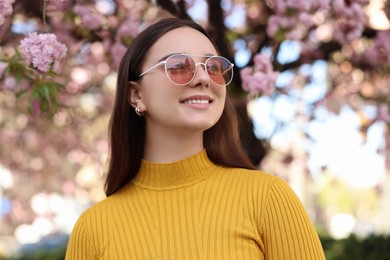 Beautiful woman in sunglasses near blossoming tree on spring day