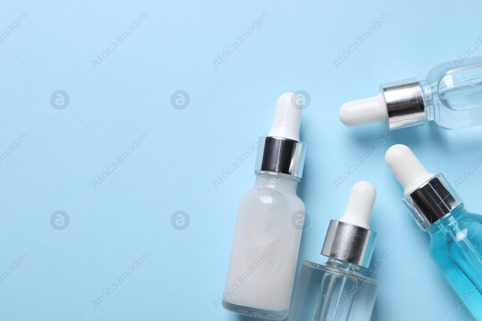 Photo of Many bottles of cosmetic serum on light blue background, flat lay. Space for text