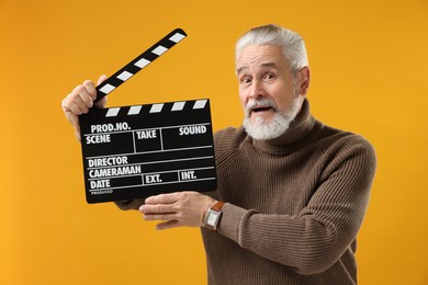 Photo of Senior actor holding clapperboard on yellow background. Film industry
