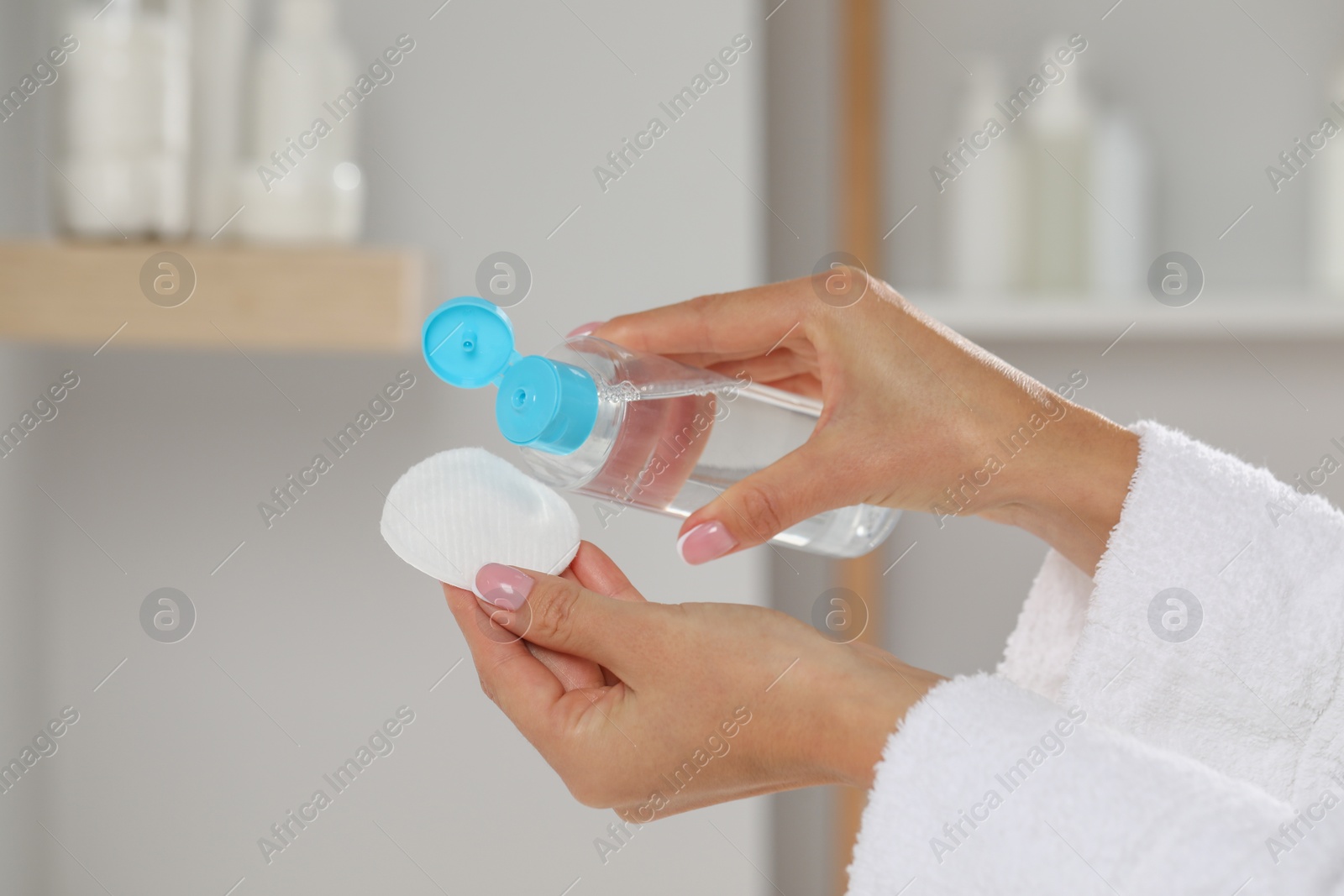 Photo of Woman pouring makeup remover from bottle onto cotton pad indoors, closeup