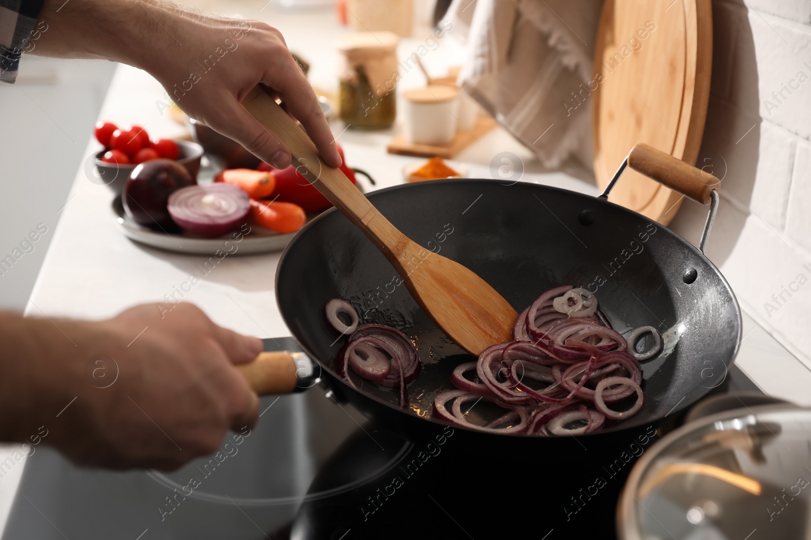 Photo of Man stirring onion slices in frying pan, closeup