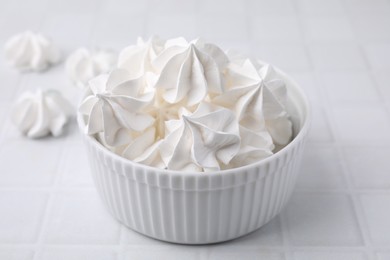 Photo of Delicious meringue cookies in bowl on white tiled table, closeup