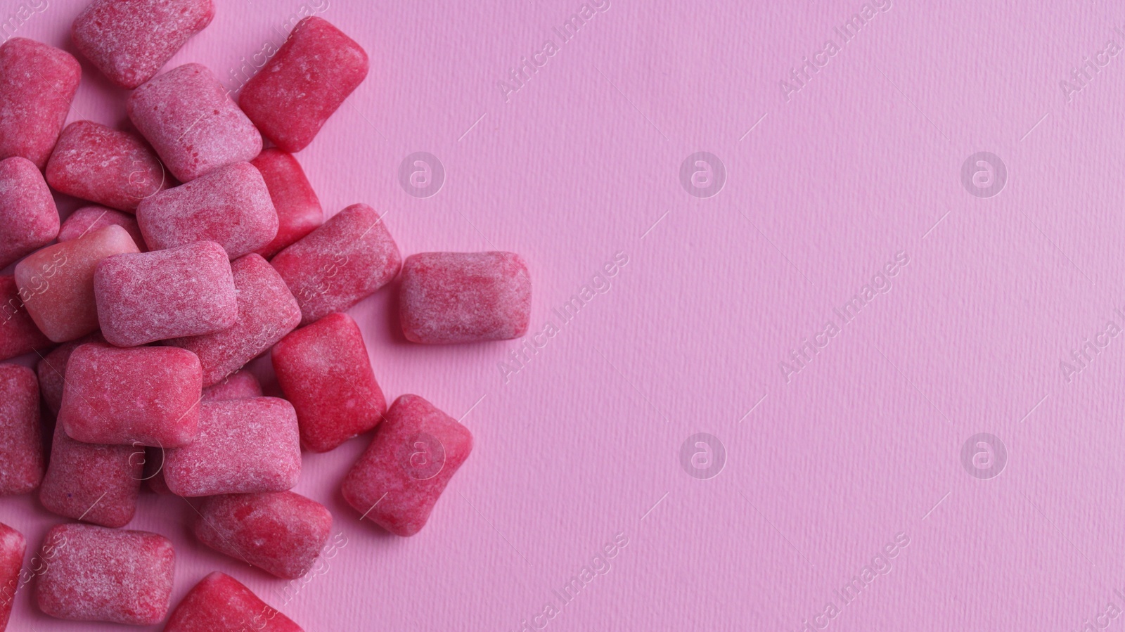 Photo of Heap of tasty sweet chewing gums on pink background, flat lay. Space for text