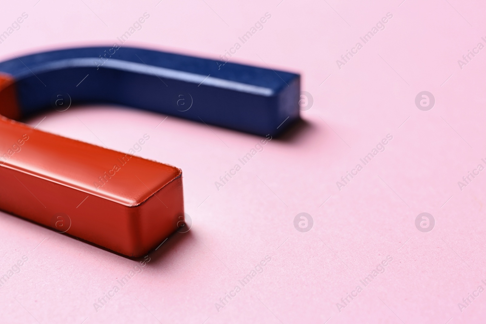 Photo of Red and blue horseshoe magnet on pink background, closeup