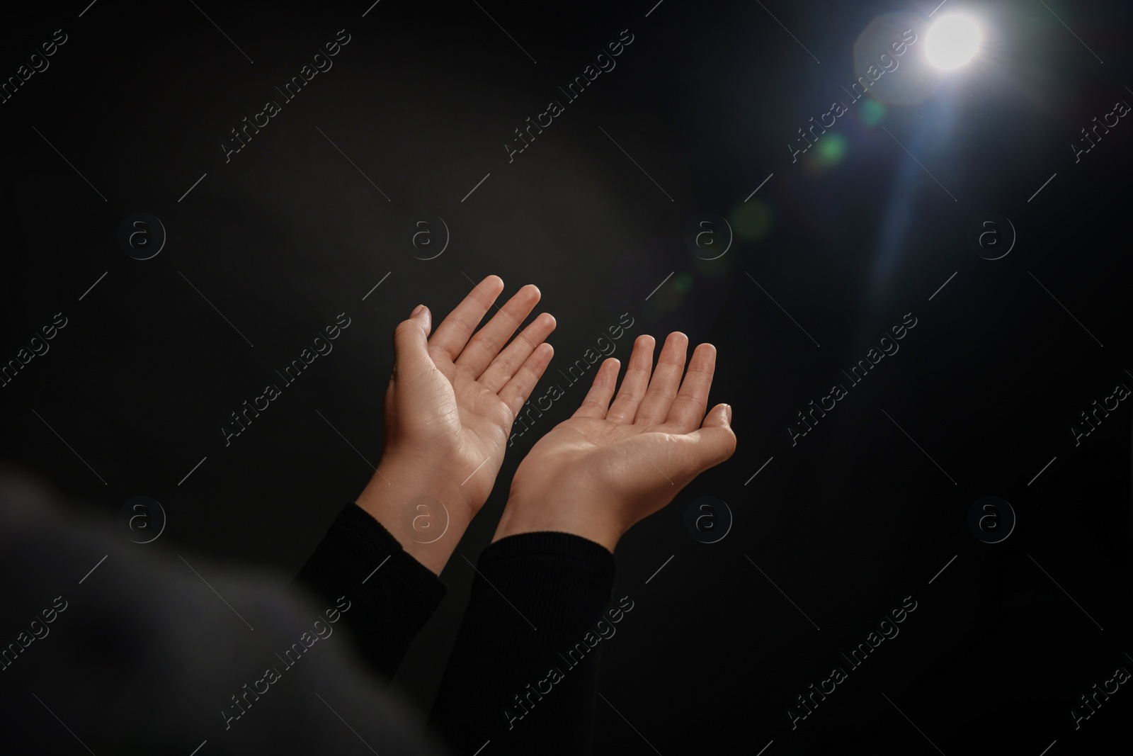 Photo of Woman stretching hands towards light in darkness, closeup