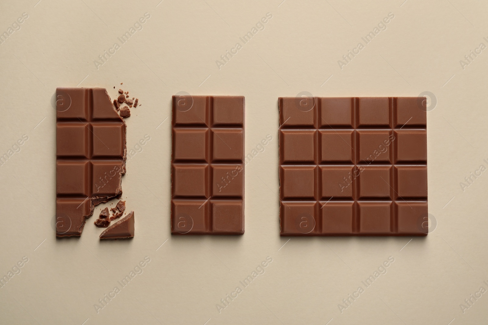 Photo of Delicious broken chocolate bar on beige background, flat lay