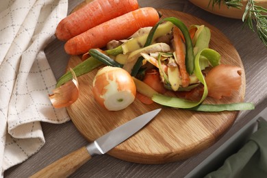 Photo of Peels of fresh vegetables and knife on wooden table, above view