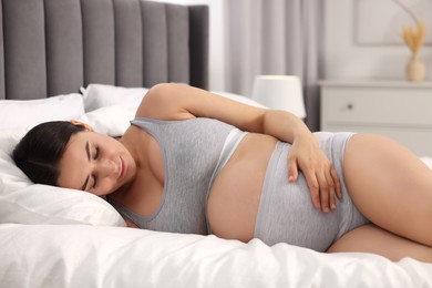 Photo of Beautiful pregnant woman in comfortable maternity underwear lying on bed at home
