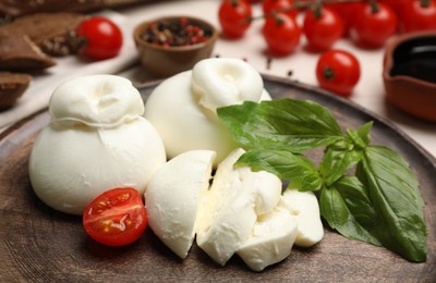 Photo of Delicious burrata cheese with basil and cut tomato on  table, closeup
