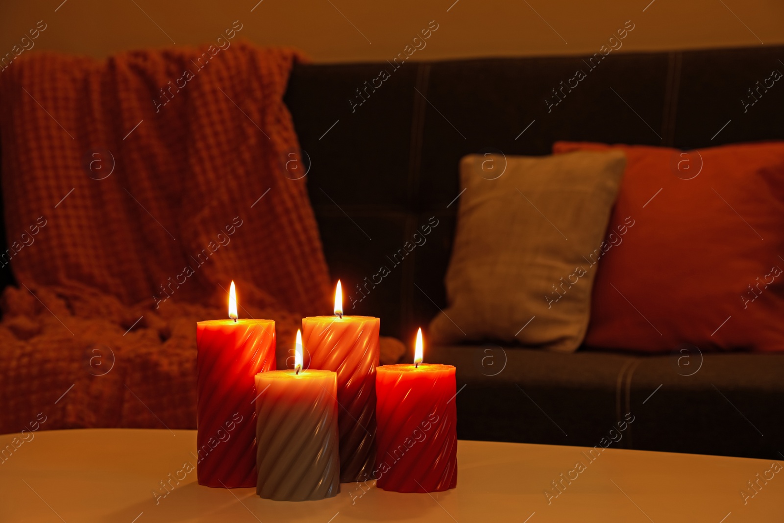 Photo of Beautiful candles on white table near sofa indoors. Cosy atmosphere