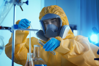 Scientist in chemical protective suit dripping reagent  into test tube at laboratory. Virus research