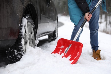 Photo of Man cleaning snow with shovel near stuck car outdoors