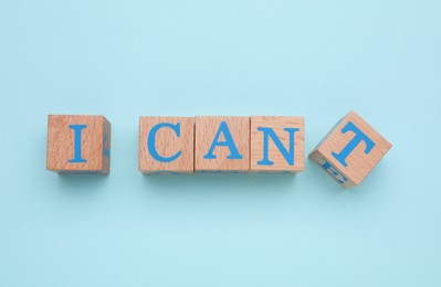 Photo of Motivation concept. Changing phrase from I Can't into I Can by removing wooden cube with letter T on light blue background, flat lay