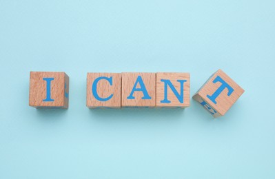 Motivation concept. Changing phrase from I Can't into I Can by removing wooden cube with letter T on light blue background, flat lay