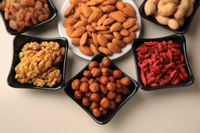 Photo of Bowls with dried fruits and nuts on beige background, above view