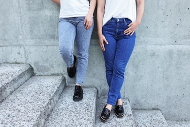 Women in stylish jeans on stairs near stone wall outdoors, closeup