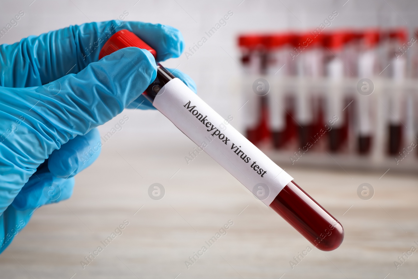 Photo of Laboratory worker holding test tube with blood sample at wooden table, closeup