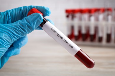 Laboratory worker holding test tube with blood sample at wooden table, closeup