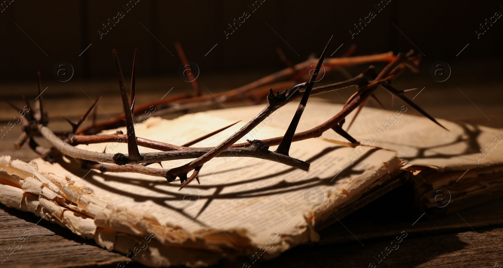 Photo of Crown of thorns and Bible on wooden table, closeup