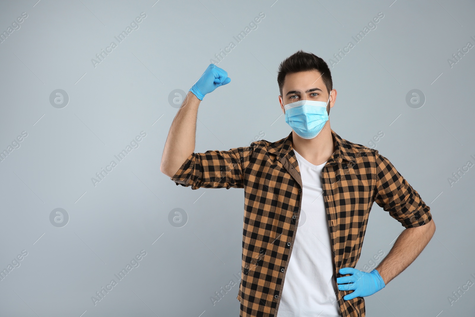 Photo of Man with protective mask and gloves showing muscles on light grey background, space for text. Strong immunity concept
