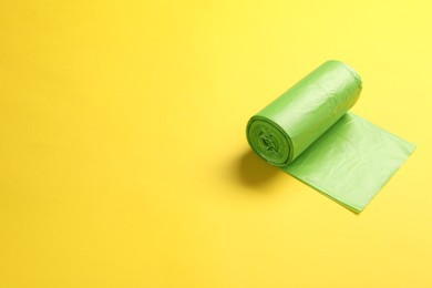 Photo of Roll of green garbage bags on yellow background, space for text