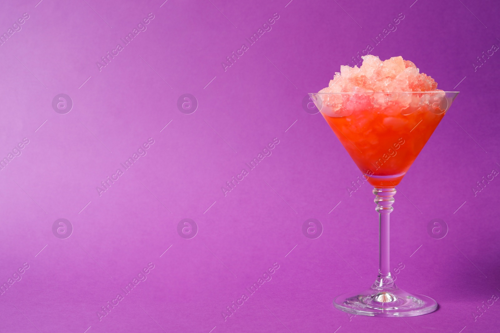 Photo of Shaving ice in martini glass on violet background, space for text