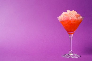 Photo of Shaving ice in martini glass on violet background, space for text