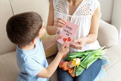 Photo of Happy woman receiving flowers and greeting card from her son at home. Mother's day celebration