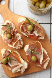 Photo of Tasty sandwiches with cured ham, rosemary and olives on tiled table, top view