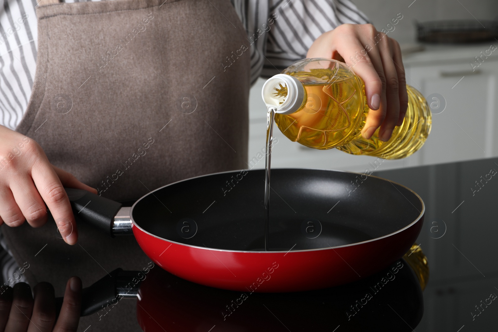 Photo of Woman pouring cooking oil from bottle into frying pan on stove, closeup