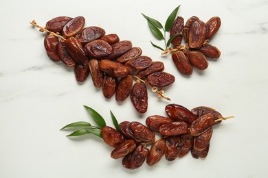 Photo of Branches with sweet dried dates and green leaves on white marble table, flat lay