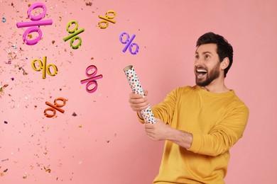 Image of Discount offer. Happy man blowing up party popper on pink background. Confetti and percent signs in air