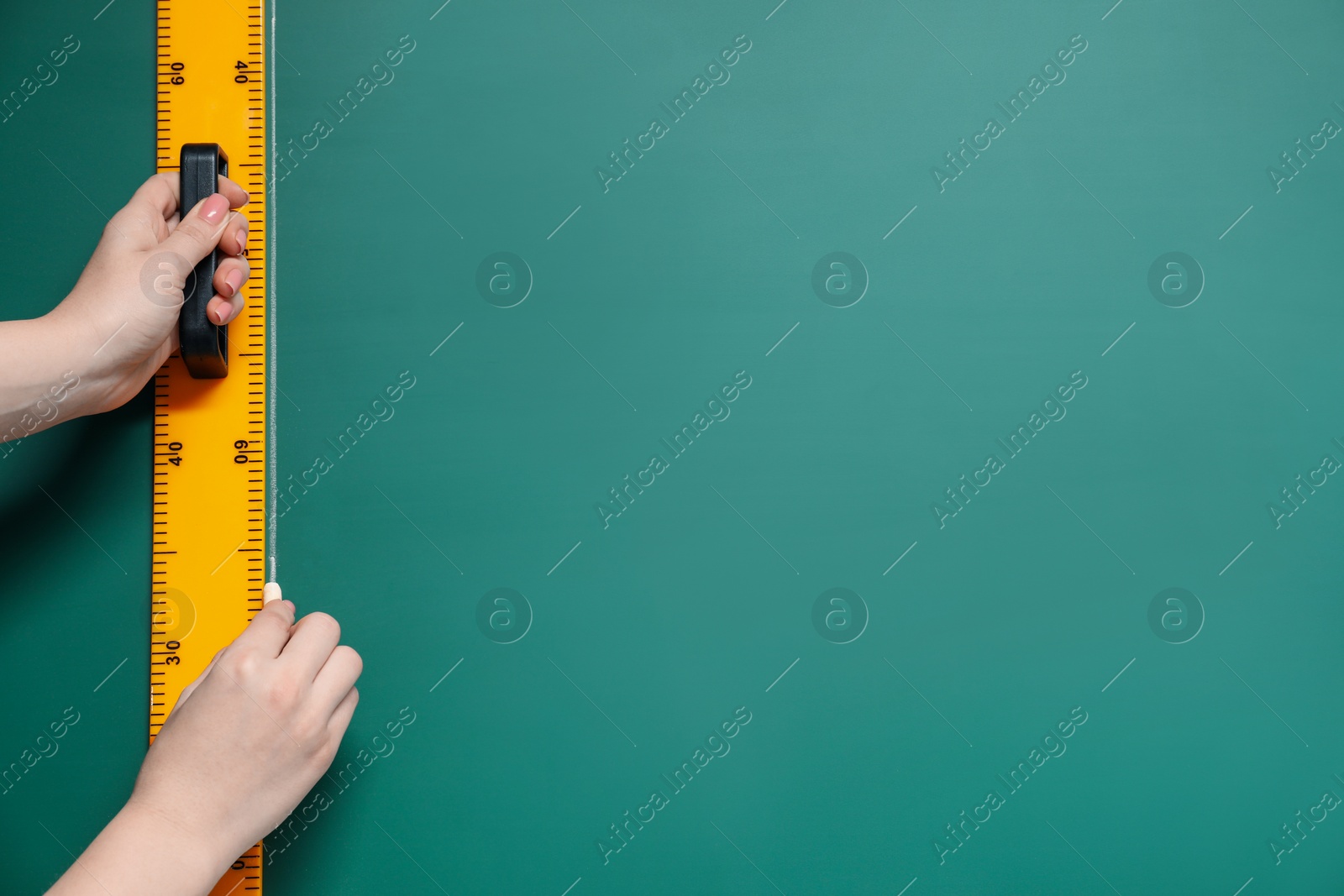 Photo of Woman drawing with chalk and ruler on green board, closeup. Space for text