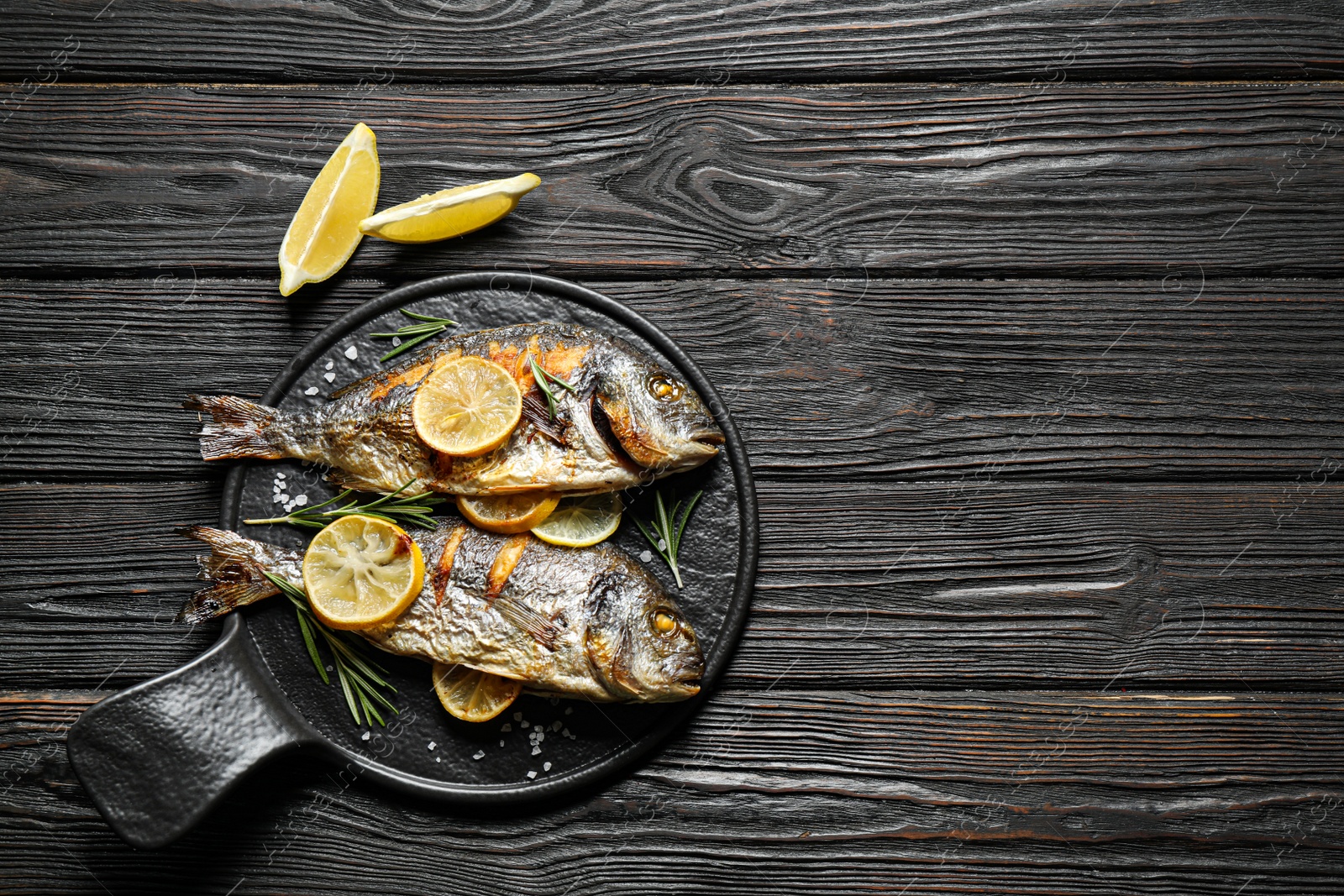 Photo of Delicious roasted fish with lemon on black wooden table, flat lay. Space for text