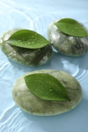 Photo of Spa stones and green leaves on light blue background, closeup