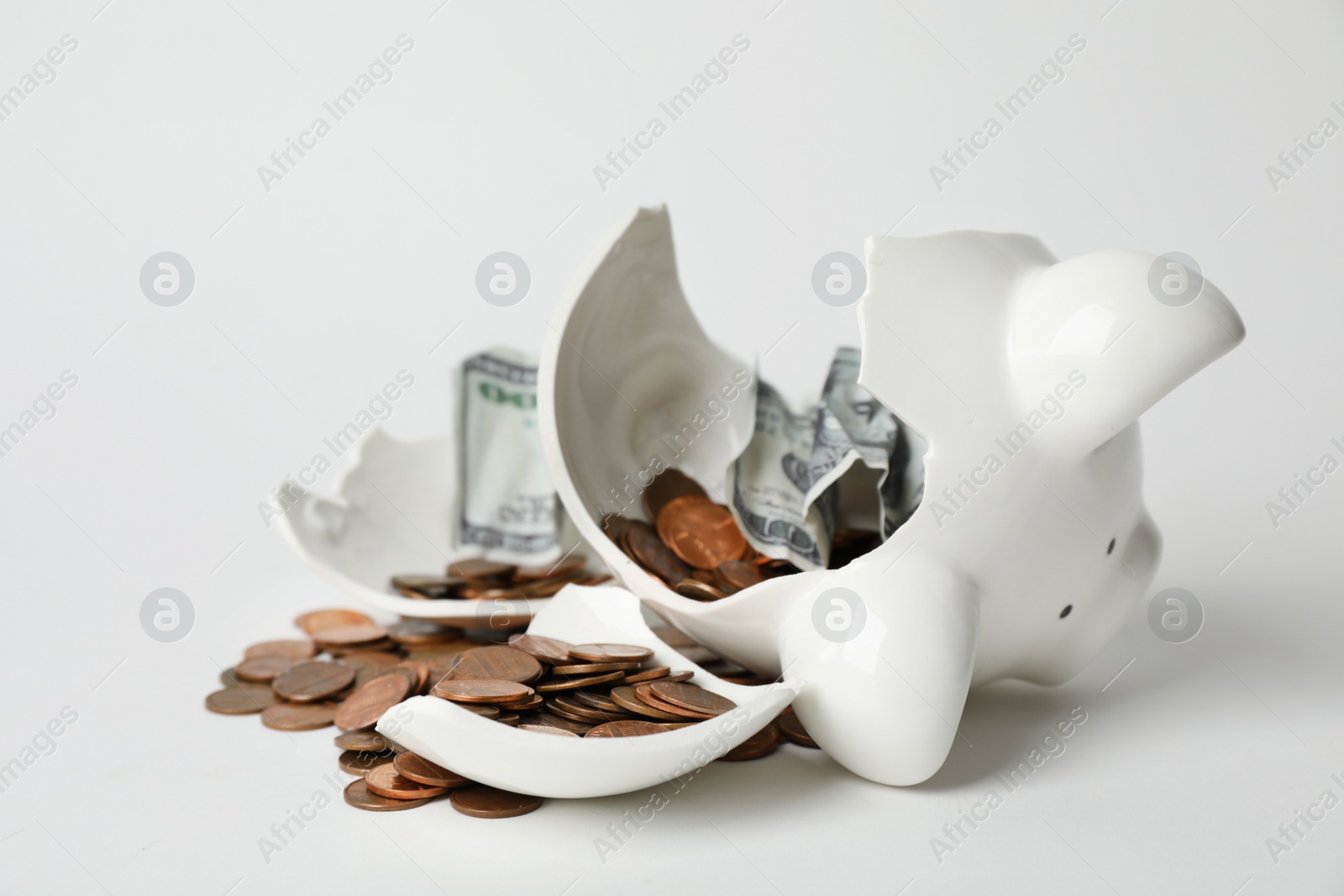 Photo of Broken piggy bank with coins and banknotes on light background