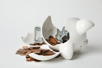 Broken piggy bank with coins and banknotes on light background