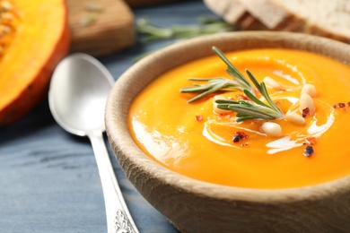 Photo of Delicious pumpkin soup in bowl on blue wooden table, closeup