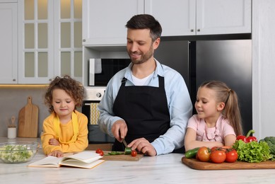 Photo of Happy man with his daughters cooking by recipe book in kitchen